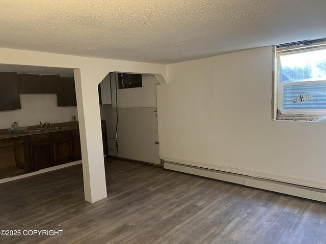 basement with a baseboard heating unit, a sink, arched walkways, a textured ceiling, and dark wood finished floors