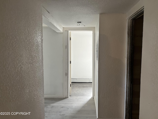 hall featuring a textured wall, wood finished floors, a baseboard heating unit, and a textured ceiling