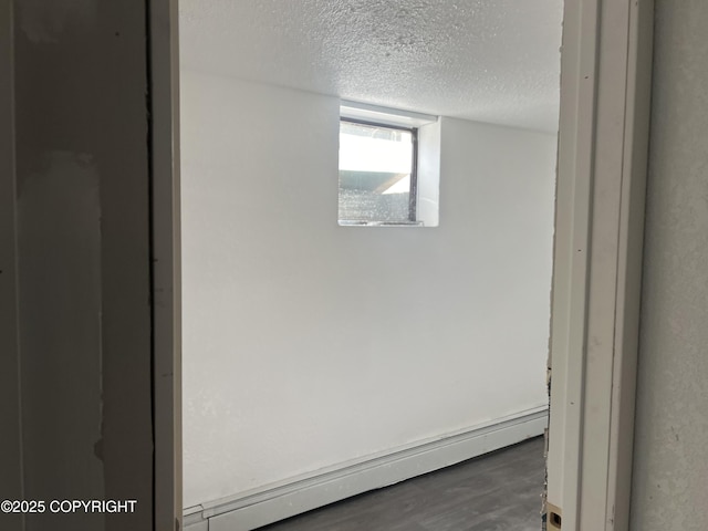 detailed view of a baseboard heating unit, a textured ceiling, and wood finished floors