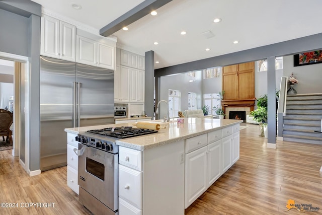 8100 Sky Mountain Ln, Anchorage, AK 99502 - kitchen featuring high end appliances, white cabinets, light wood finished floors, a kitchen island with sink, and recessed lighting