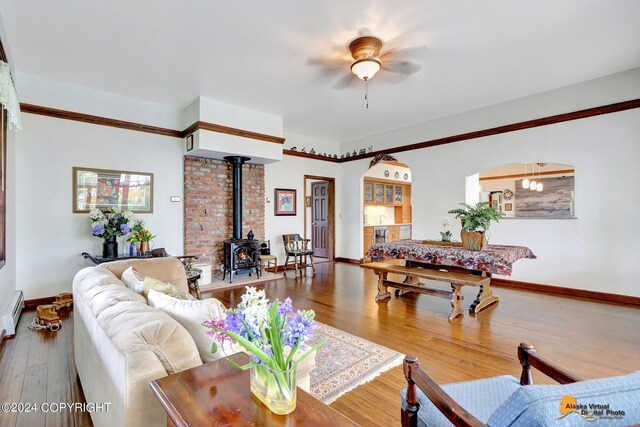 living room with a wood stove, wood-type flooring, baseboard heating, and ceiling fan