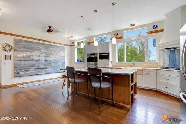 kitchen with appliances with stainless steel finishes, dark wood-type flooring, white cabinets, a kitchen island, and pendant lighting