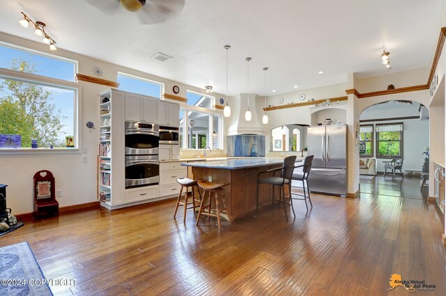 kitchen featuring pendant lighting, wood-type flooring, a center island, white cabinets, and stainless steel appliances