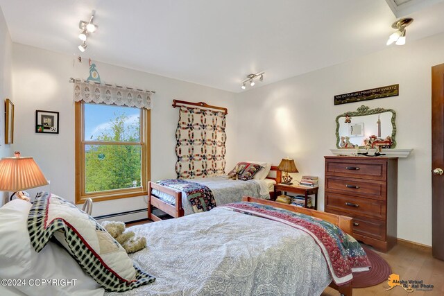 bedroom with track lighting, baseboard heating, and hardwood / wood-style floors