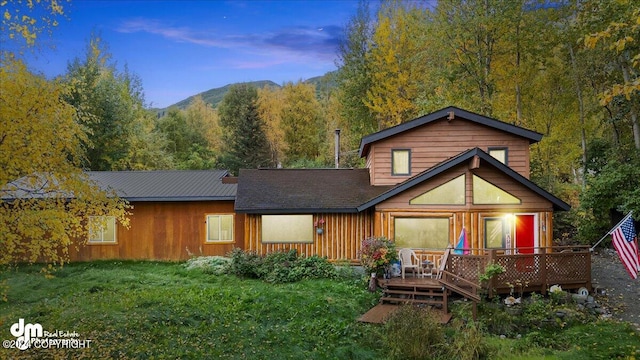 back house at dusk featuring a deck with mountain view and a yard