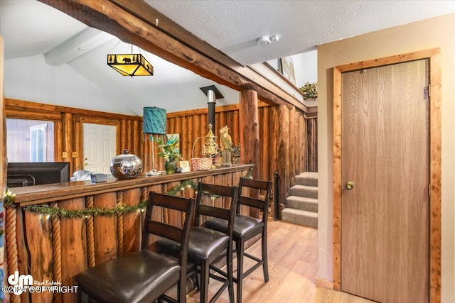 interior space with light wood-type flooring, vaulted ceiling with beams, a textured ceiling, and wood walls