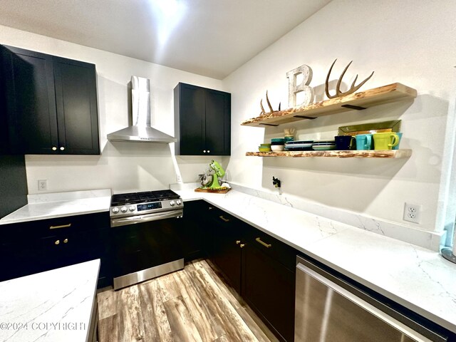 kitchen featuring wall chimney exhaust hood, light stone countertops, stainless steel appliances, and light hardwood / wood-style flooring