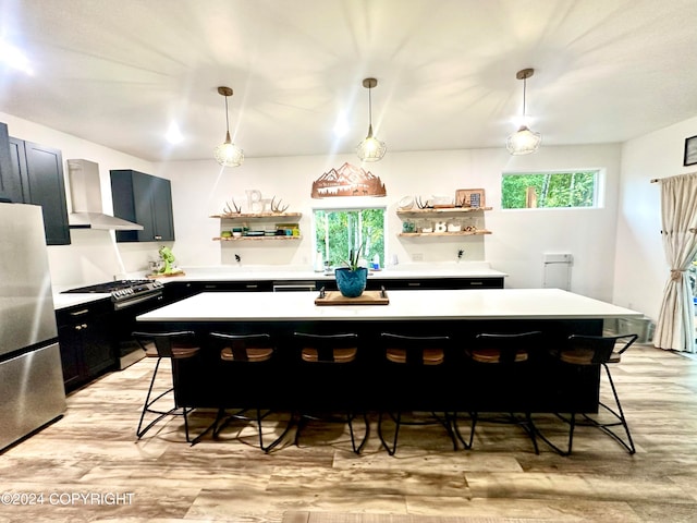 kitchen with a kitchen bar, stainless steel appliances, wall chimney range hood, pendant lighting, and a kitchen island