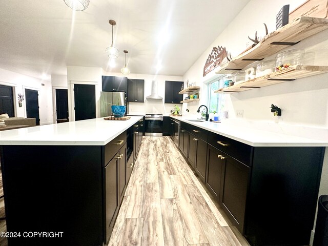 kitchen with wall chimney range hood, sink, light wood-type flooring, decorative light fixtures, and stainless steel appliances