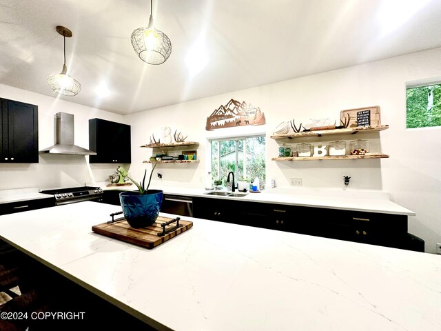 kitchen with light stone countertops, sink, stainless steel appliances, hanging light fixtures, and wall chimney range hood