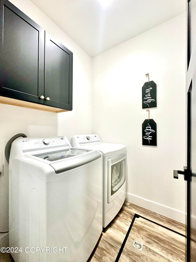 washroom featuring washing machine and dryer, light hardwood / wood-style flooring, and cabinets