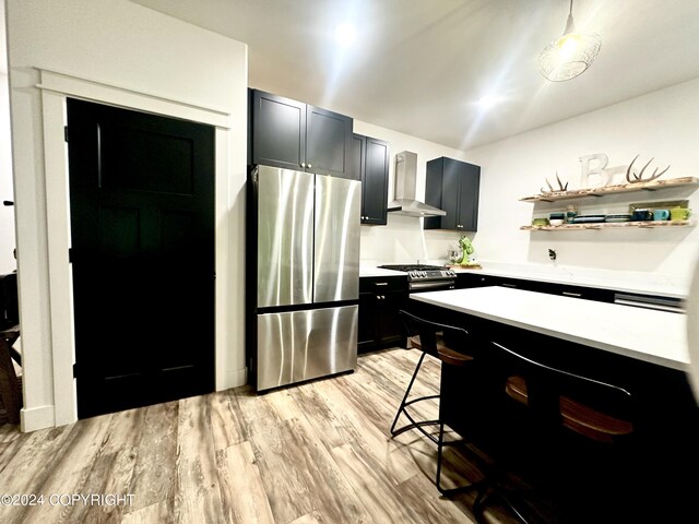 kitchen with a kitchen bar, stainless steel fridge, wall chimney range hood, light hardwood / wood-style flooring, and hanging light fixtures