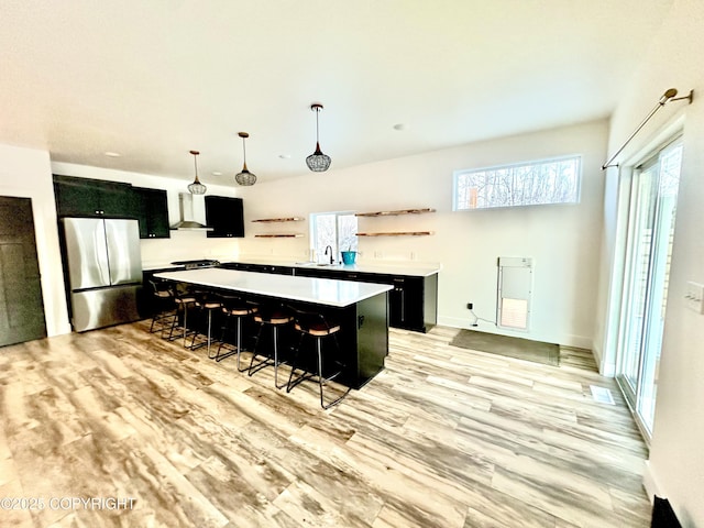 kitchen with a kitchen bar, wall chimney exhaust hood, decorative light fixtures, a center island, and stainless steel refrigerator