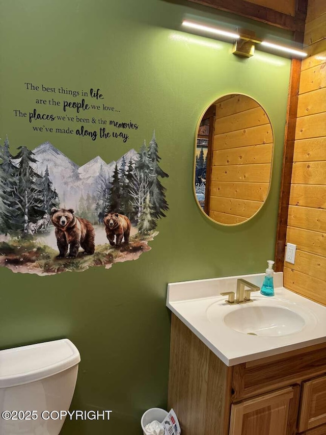 bathroom featuring toilet, wooden walls, and vanity