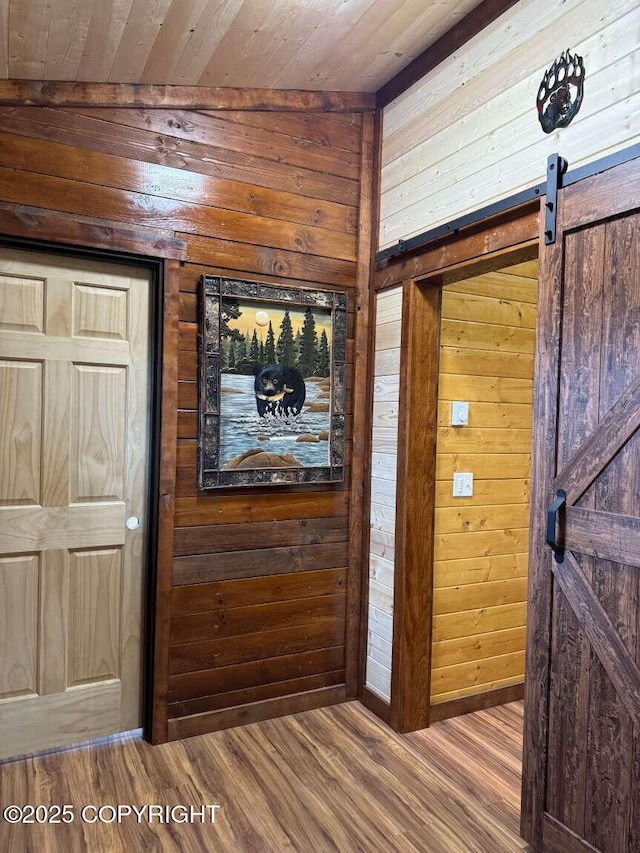 corridor with a barn door, wood walls, wooden ceiling, and wood finished floors