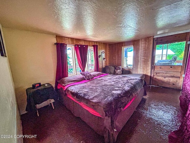 bedroom featuring a textured ceiling, dark carpet, wooden walls, and multiple windows