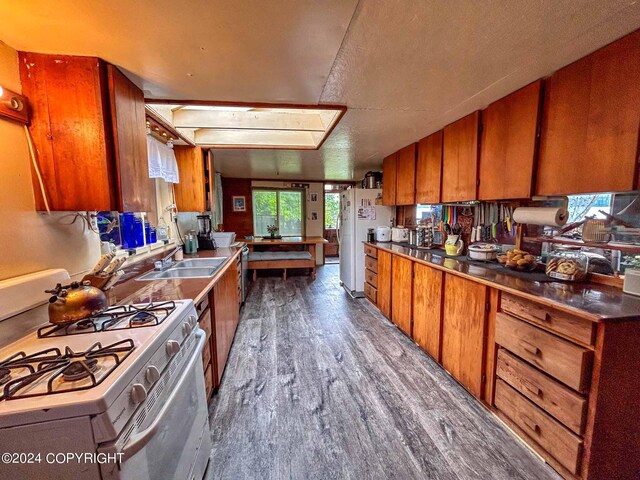 kitchen with a textured ceiling, white appliances, sink, hardwood / wood-style flooring, and a skylight