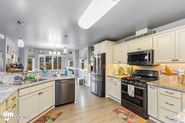 kitchen with hanging light fixtures, light wood-type flooring, appliances with stainless steel finishes, and cream cabinetry