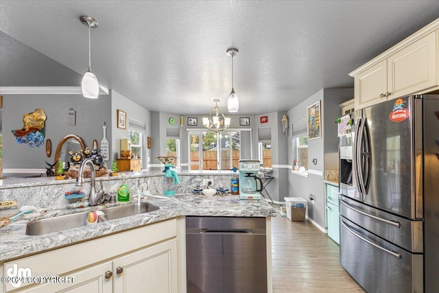 kitchen featuring cream cabinets, decorative light fixtures, light wood-type flooring, stainless steel fridge, and a textured ceiling