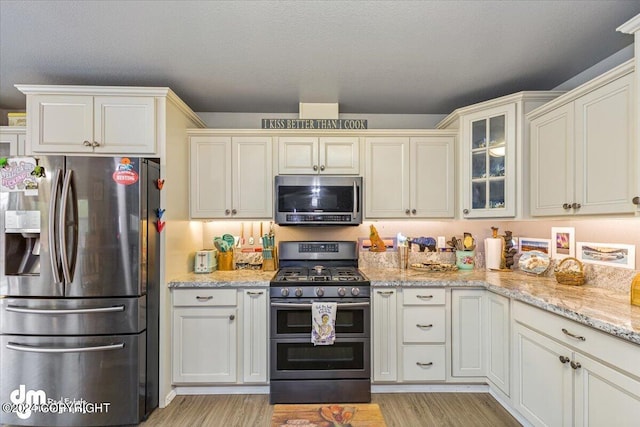 kitchen featuring appliances with stainless steel finishes, a textured ceiling, light hardwood / wood-style flooring, and light stone countertops