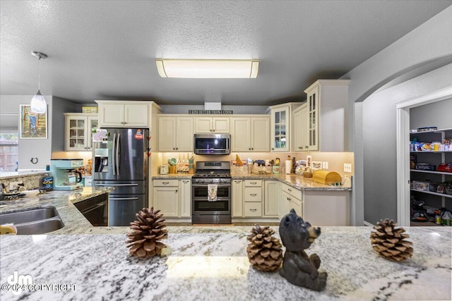 kitchen with cream cabinets, decorative light fixtures, light stone countertops, stainless steel appliances, and a textured ceiling