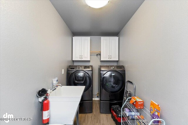 clothes washing area featuring a textured ceiling, cabinets, washing machine and clothes dryer, and light hardwood / wood-style floors