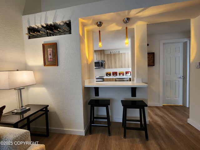 4342 Reka Dr, Anchorage, AK 99508 - kitchen featuring stainless steel appliances, dark wood-type flooring, a breakfast bar, light countertops, and hanging light fixtures