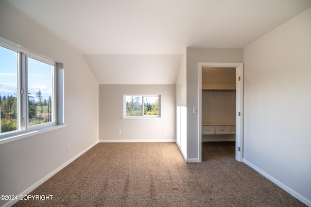 unfurnished bedroom with lofted ceiling, a spacious closet, dark carpet, and a closet