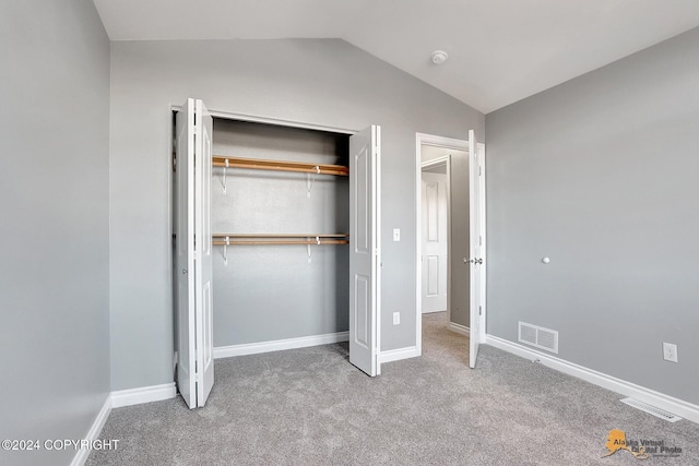 unfurnished bedroom featuring vaulted ceiling, light colored carpet, and a closet