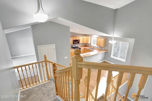 stairs featuring high vaulted ceiling, an inviting chandelier, sink, and carpet flooring