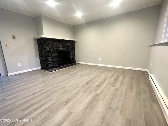 unfurnished living room with a stone fireplace, a baseboard radiator, and light wood-type flooring