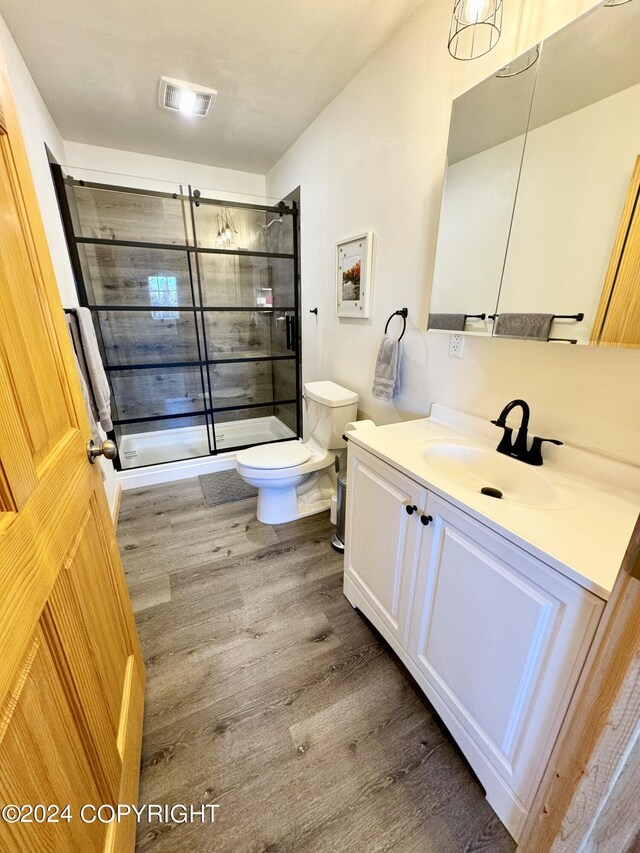 bathroom with wood-type flooring, a shower with door, vanity, and toilet