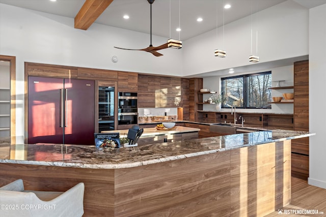 kitchen featuring beam ceiling, stone counters, sink, hanging light fixtures, and stainless steel appliances