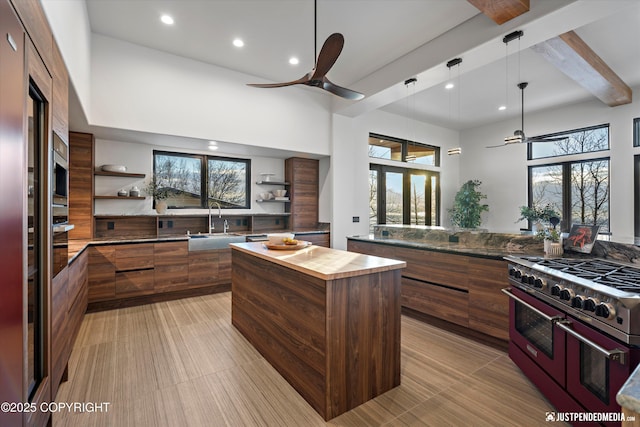 kitchen with ceiling fan, a center island, double oven range, and a towering ceiling