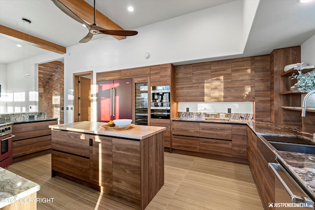 kitchen featuring sink, ceiling fan, appliances with stainless steel finishes, beamed ceiling, and a kitchen island