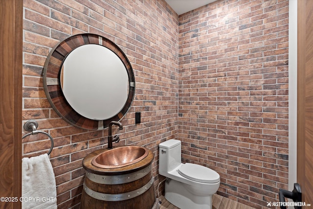 bathroom with vanity, toilet, and brick wall