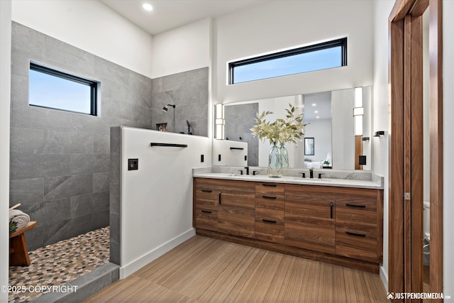 bathroom with a tile shower, vanity, and a healthy amount of sunlight