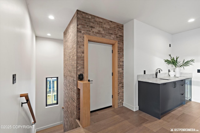 bar featuring gray cabinets, beverage cooler, sink, and brick wall