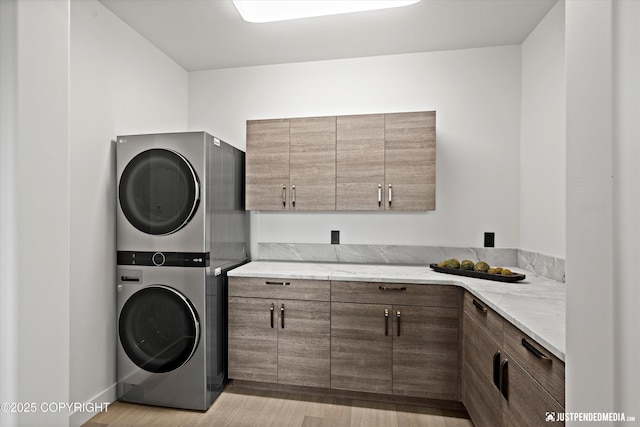 clothes washing area featuring cabinets, light hardwood / wood-style flooring, and stacked washer / dryer