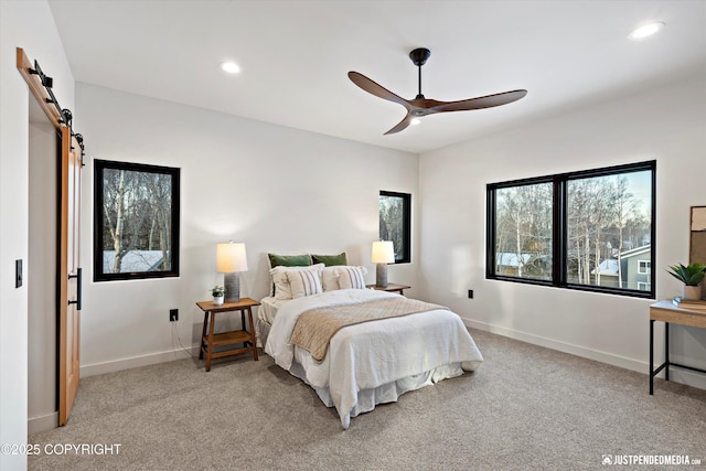 bedroom with ceiling fan, a barn door, and light colored carpet