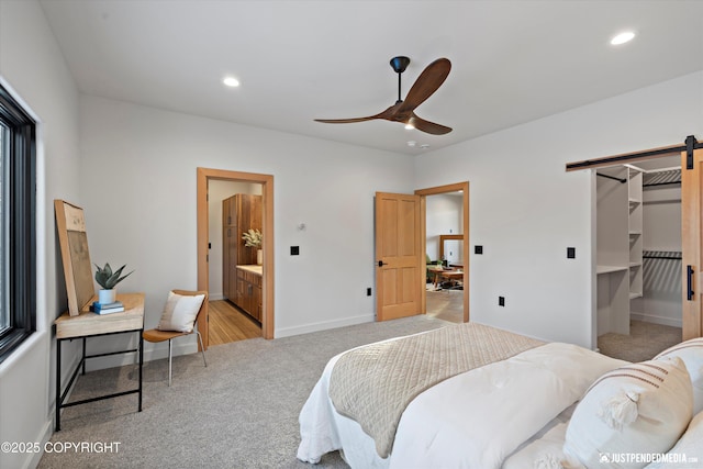 carpeted bedroom featuring a walk in closet, ceiling fan, a barn door, connected bathroom, and a closet