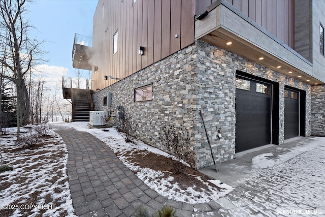 view of snow covered exterior featuring central AC unit and a garage