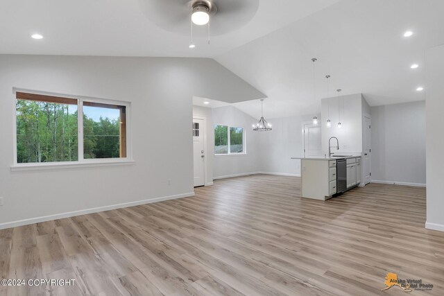 unfurnished living room featuring sink, ceiling fan with notable chandelier, vaulted ceiling, and light hardwood / wood-style flooring