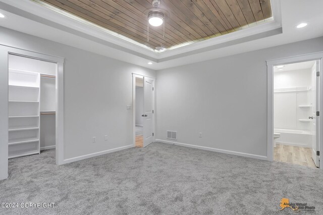 unfurnished bedroom featuring connected bathroom, a tray ceiling, a spacious closet, and light colored carpet