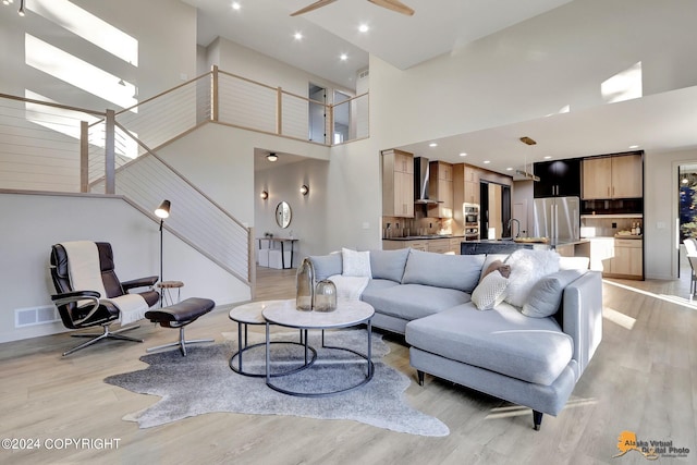 living room with a high ceiling, ceiling fan, and light hardwood / wood-style flooring