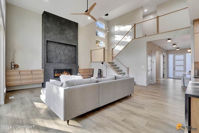 living room featuring a high ceiling, a large fireplace, ceiling fan, and light hardwood / wood-style flooring