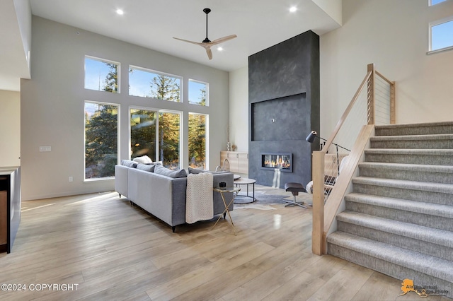 living room featuring a fireplace, a towering ceiling, ceiling fan, and light hardwood / wood-style flooring