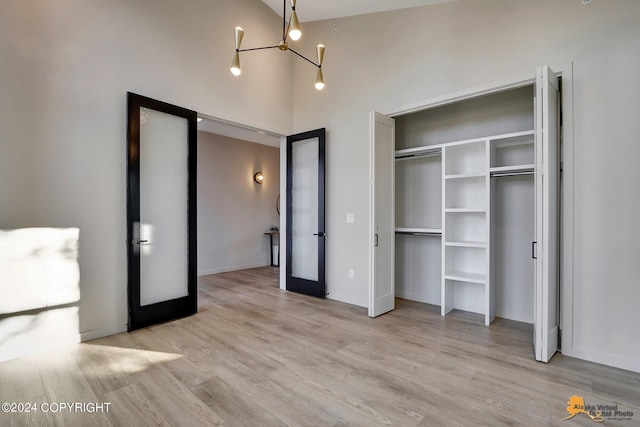 unfurnished bedroom featuring french doors, a closet, an inviting chandelier, a towering ceiling, and light hardwood / wood-style floors