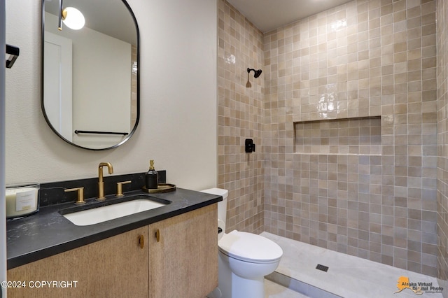 bathroom with a tile shower, vanity, and toilet