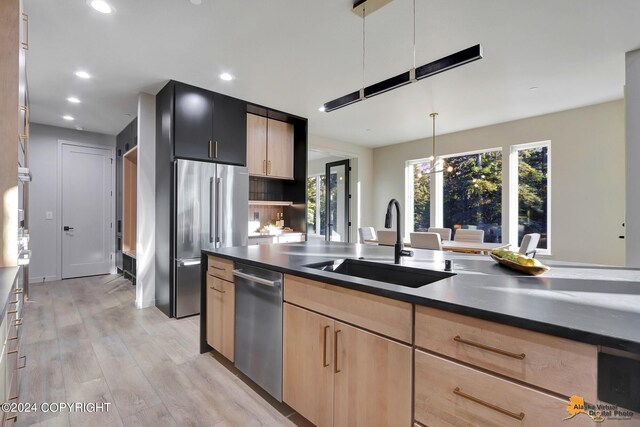 kitchen with light brown cabinets, pendant lighting, stainless steel appliances, light hardwood / wood-style flooring, and sink